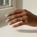 African American woman's French manicure hand wearing ATORI Lumini pink teardrop gemstone gold plated adjustable ring on a neutral background